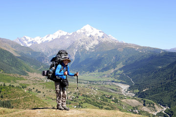 hiker with backpack and trekking sticks standing in the background of mountain landscape.