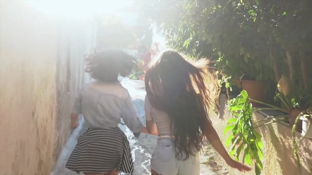Two girls running across sunny street in Greece