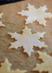 Christmas cookies thinly rolled and cut out in star shape saying the German words Frohes Fest, which means Happy Holidays, on parchment paper on baking sheet about to go in the oven to be baked
