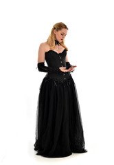 full length portrait of a blonde girl wearing black gothic gown. standing pose, isolated on white background.