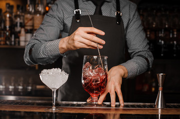 Barman stirring an alcoholic drink with ice in a cocktail glass
