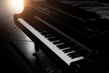 Black shiny grand piano with white keyboard in dark tone