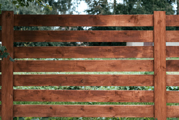 Wooden fence, a pen for horses, brown of boards. Green grass and trees against the background of boards. Summer autumn day in nature.