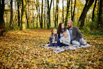 Fototapeta premium Happy caucasian family of mom dad and little girl with boy sitting on plaid at majestic autumn fall forest.