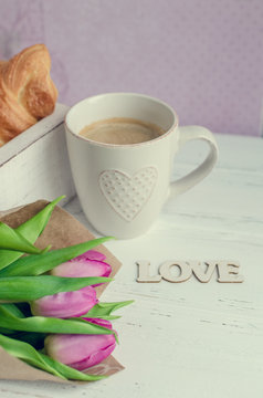 Cup of coffee with croissants, bouquet of pink tulips and wooden word LOVE