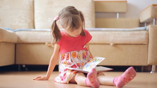 Little girl reads book sitting on the floor