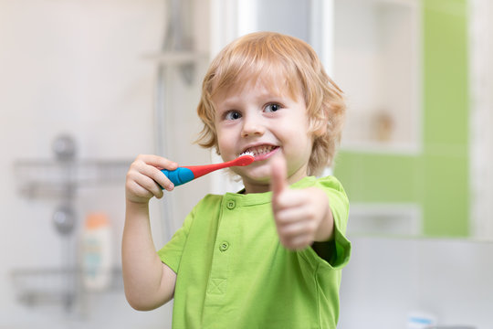 Little boy brushing his teeth in the bathroom. Smiling child holding toothbrush and showing thumbs up.