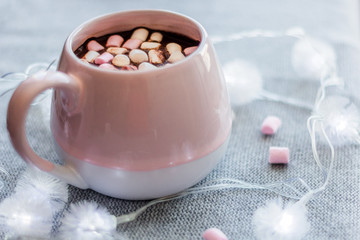 Obraz na płótnie Canvas hot chocolate pink ceramic mug marshmallows and garland gray knitted background