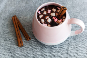 hot chocolate  pink ceramic mug marshmallows and cinnamon sticks gray knitted background