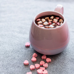 hot chocolate  pink ceramic mug marshmallows and heart shaped pink chocolate candies  gray knitted background