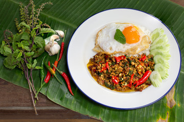 Spicy Stir fried chicken chopping with basil leaves and fried egg Thai food in white dish on green banana leaf