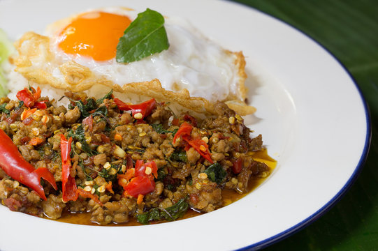 Spicy Stir fried chicken chopping with basil leaves and fried egg Thai food in white dish on green banana leaf