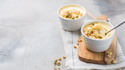 Classic cheesecake in small ceramic jars with nuts and honey on light concrete background and wooden board. The most delicious dessert or the perfect healthy breakfast!)