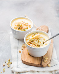 Classic cheesecake in small ceramic jars with nuts and honey on light concrete background and wooden board. The most delicious dessert or the perfect healthy breakfast!)