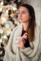 Young woman relaxing with a mug of coffee as she cuddles up in warm blanket on ancient commode. Her eyes closed and serene expression