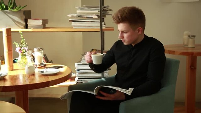 Young office Guy leaf through the Glossy Fashion Magazine sitting at the Table