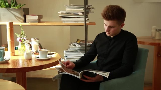Young office Guy leaf through the Glossy Fashion Magazine sitting at the Table