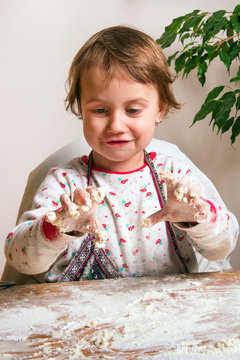 A cute little girl with her hands in dough prepares her first delicious meal in flour - a pie and dumplings