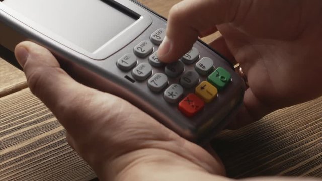Man's hand pushing the button and swipe credit card payment on pos terminal standing on wooden desk.