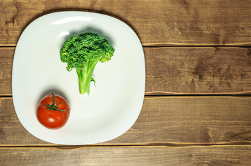 Tomato and broccoli on a plate on a wooden background. A white plate. A series of snapshots of healthy nutrition.