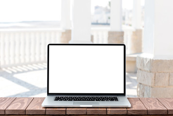 Modern laptop with empty white screen on wooden table against blurred urban background