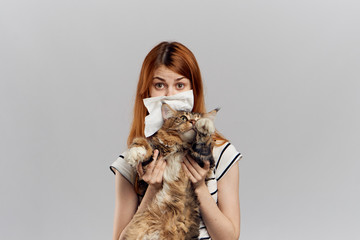 young beautiful woman holding a cat on a gray background, allergic to pets, runny nose