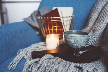 Cozy winter weekend at home. Morning with coffee or cocoa, books, warm knitted blanket and nordic style chair. Hygge concept.