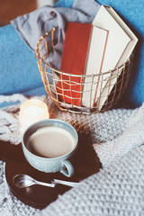 Cozy winter weekend at home. Morning with coffee or cocoa, books, warm knitted blanket and nordic style chair. Hygge concept.