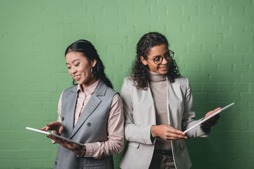african american and asian businesswomen using digital tablets in front of green wall