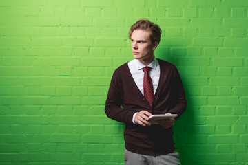 young businessman with digital tablet in front of green wall