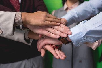 cropped view of business team holding hands together in front of green wall