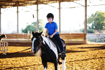 Portrait of little boy riding a horse. First lessons of horseback riding.