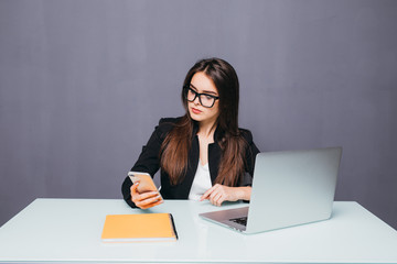 Young smiling business woman using smartphone near computer in office