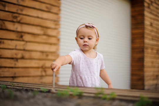 Cute little girl dressed in pretty pink dress playing outdoors with stick