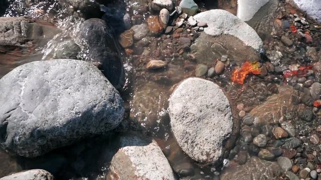 Panning shot of big and small stones in fast running water on sunny day. Slow motion