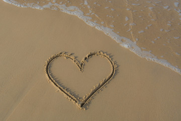 Heart drawn on the beach sand with sea foam and wave