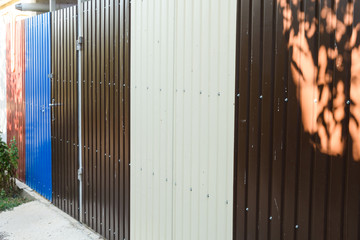 Colorful fence made of corrugated metal around a suburban area with a gate and a small ornamental green areas, zinc sheet closeup