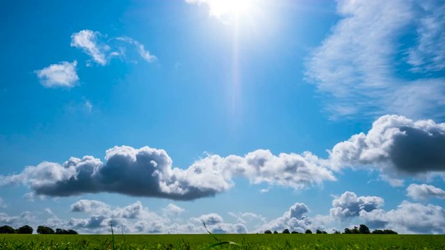 Time lapse of a bright sunny day with layered clouds moving across a meadow in summer