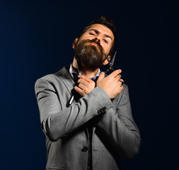 Man with long beard holds shaving razor and scissors.