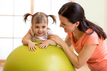 Mother with happy kid doing exercises with gymnastic ball at fitness class. Concept of caring for the baby's health.