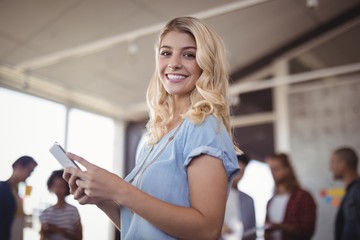 Smiling businesswoman holding mobile phone in creative office