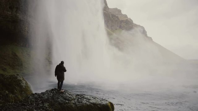 Young tourists with action camera near the Gljufrabui waterfall in Iceland. Man looking on famous sight of North nature.