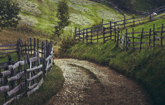 Dirt road and rustic wooden fences in a traditional Transylvanian village, Brasov county, Romania.