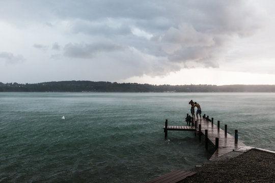 Two men standing in thunderstorm on jetty at Lake Starnberg, Germany