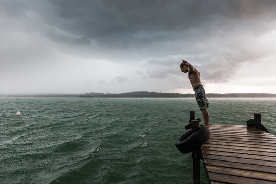 Man leaning into thunderstorm on jetty at Lake Starnberg, Germany