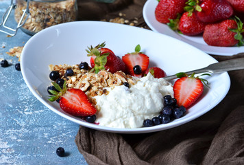 Good morning! Breakfast with yoghurt, granola and strawberries on a blue, concrete background.