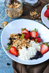 Good morning! Breakfast with yoghurt, granola and strawberries on a blue, concrete background.