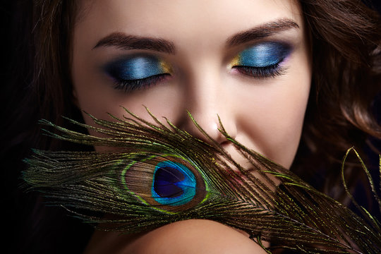 Portrait of beautiful brunette woman on black background with eyes closed and  peacock feather in hand