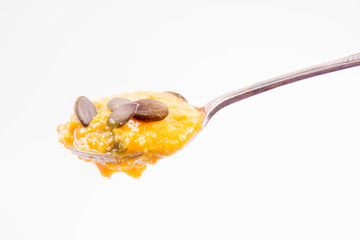 Pumpkin and carrot soup decorated with pumpkin seeds on a spoon on a white background