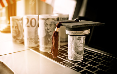 Concept of international graduate study, graduation black cap on pile of foreign money US dollars,...